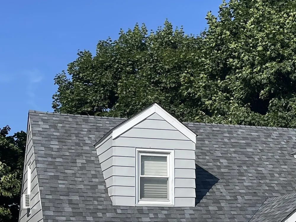 A cape cod home with a new gray architectural shingle roof and a white dormer